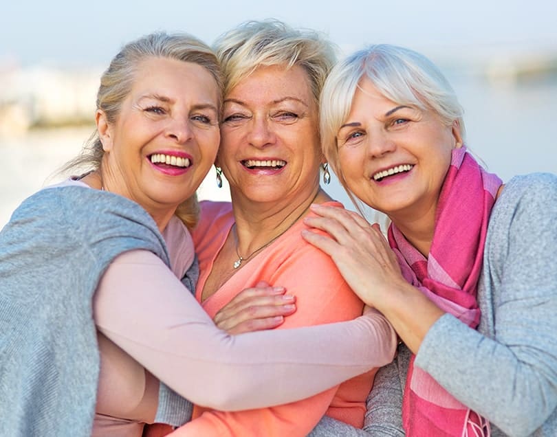Three women smile and embrace each other in a group hug
