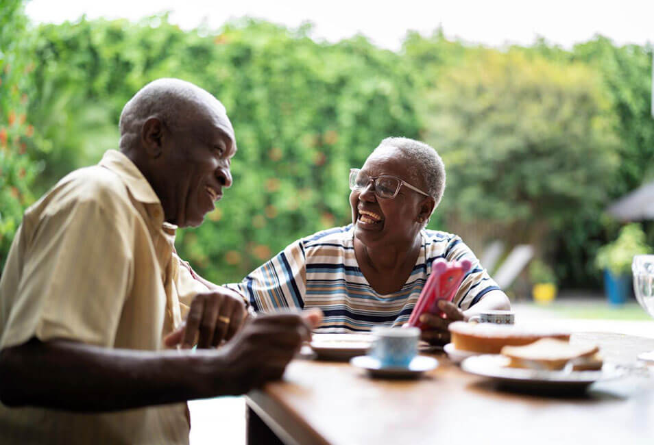 An older man and woman laugh together while enjoying a meal