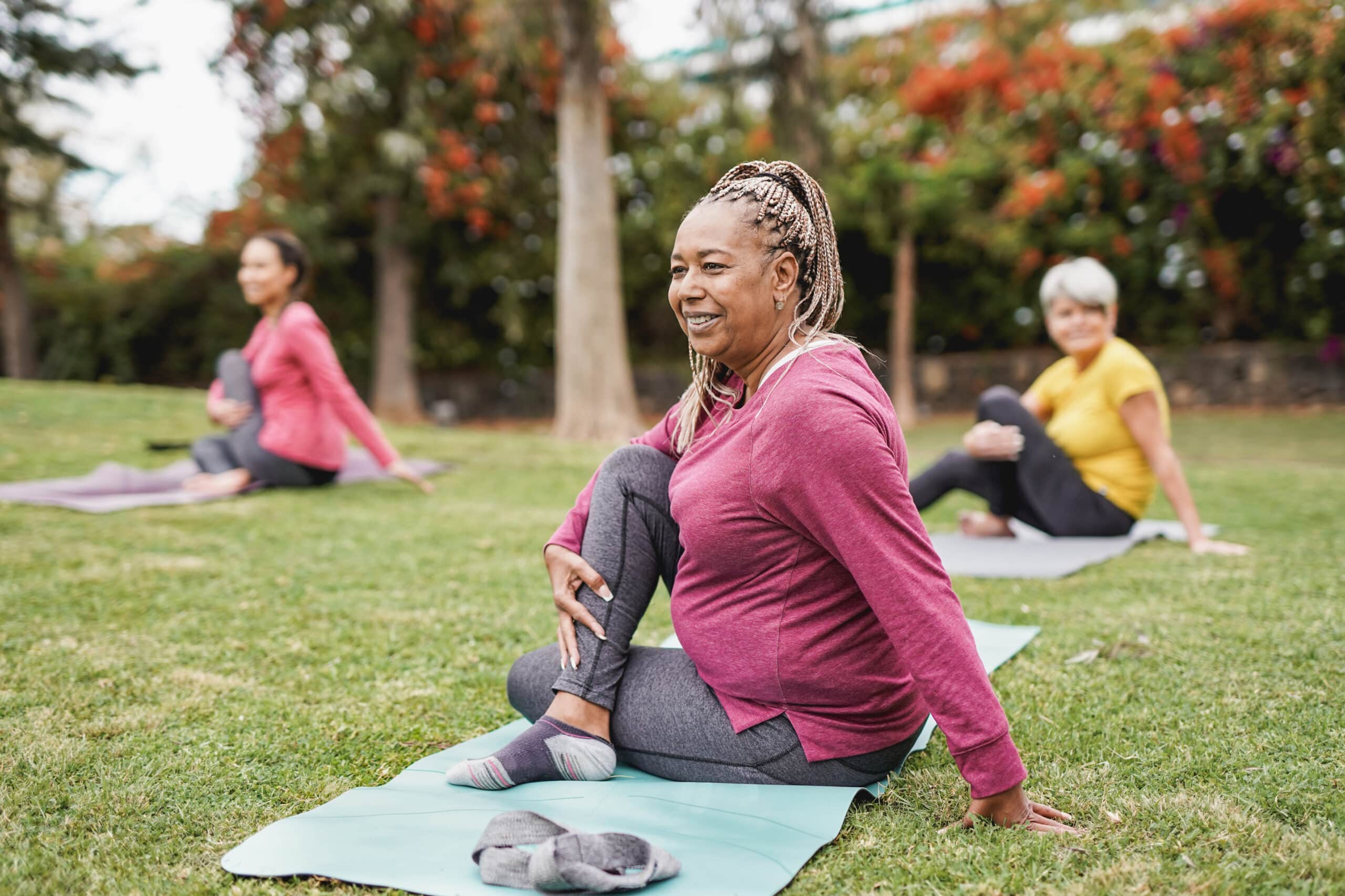 Three senior women participating in an outdoor yoga session outside their independent living facility.