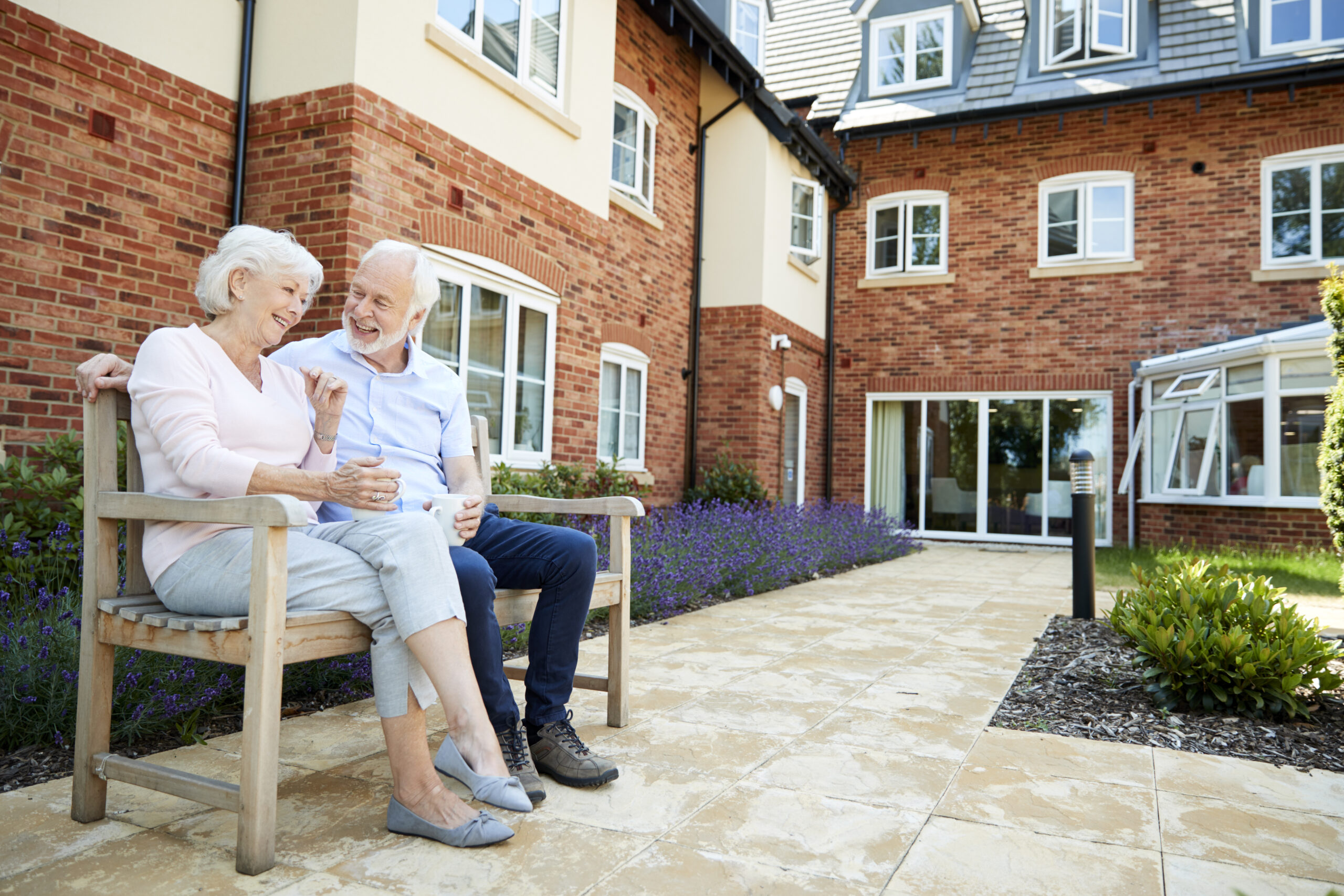 Two seniors sitting on a bench, celebrating their new, affordable accommodations.