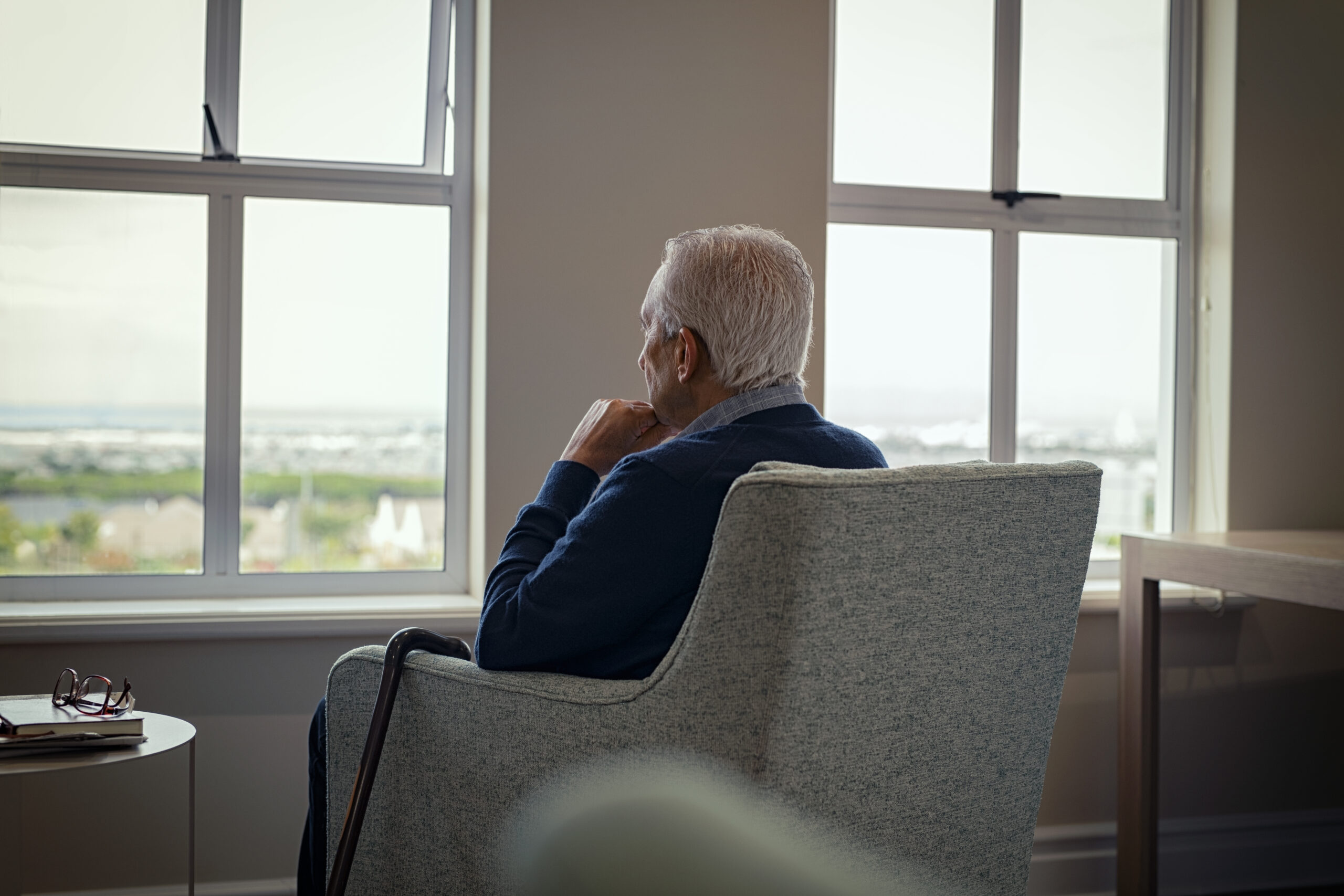 An isolated senior sitting in a chair and looking out the window.