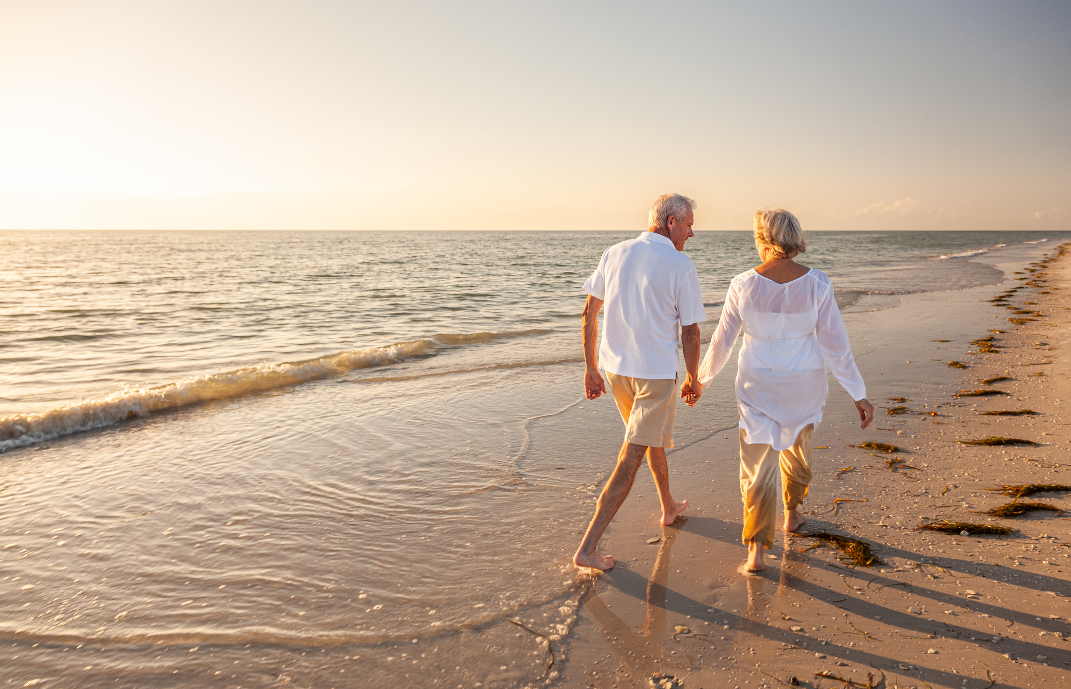 Two senior travelers walking on the beach together.
