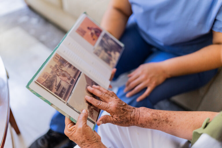 Senior looking through nostalgic photos with caregiver at a memory care community