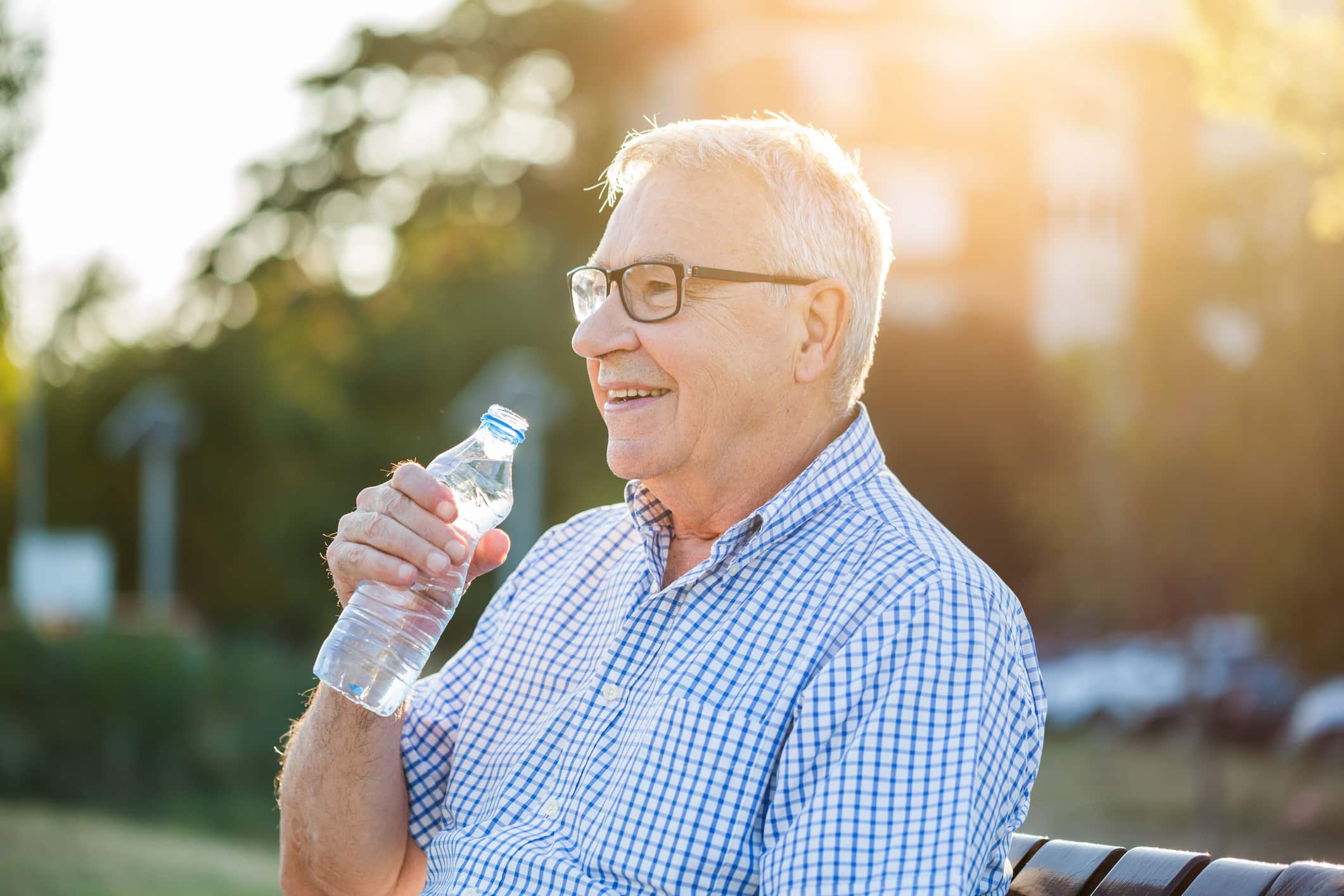 A happy older man drinking from a bottle of water after learning about the importance of hydration for seniors.