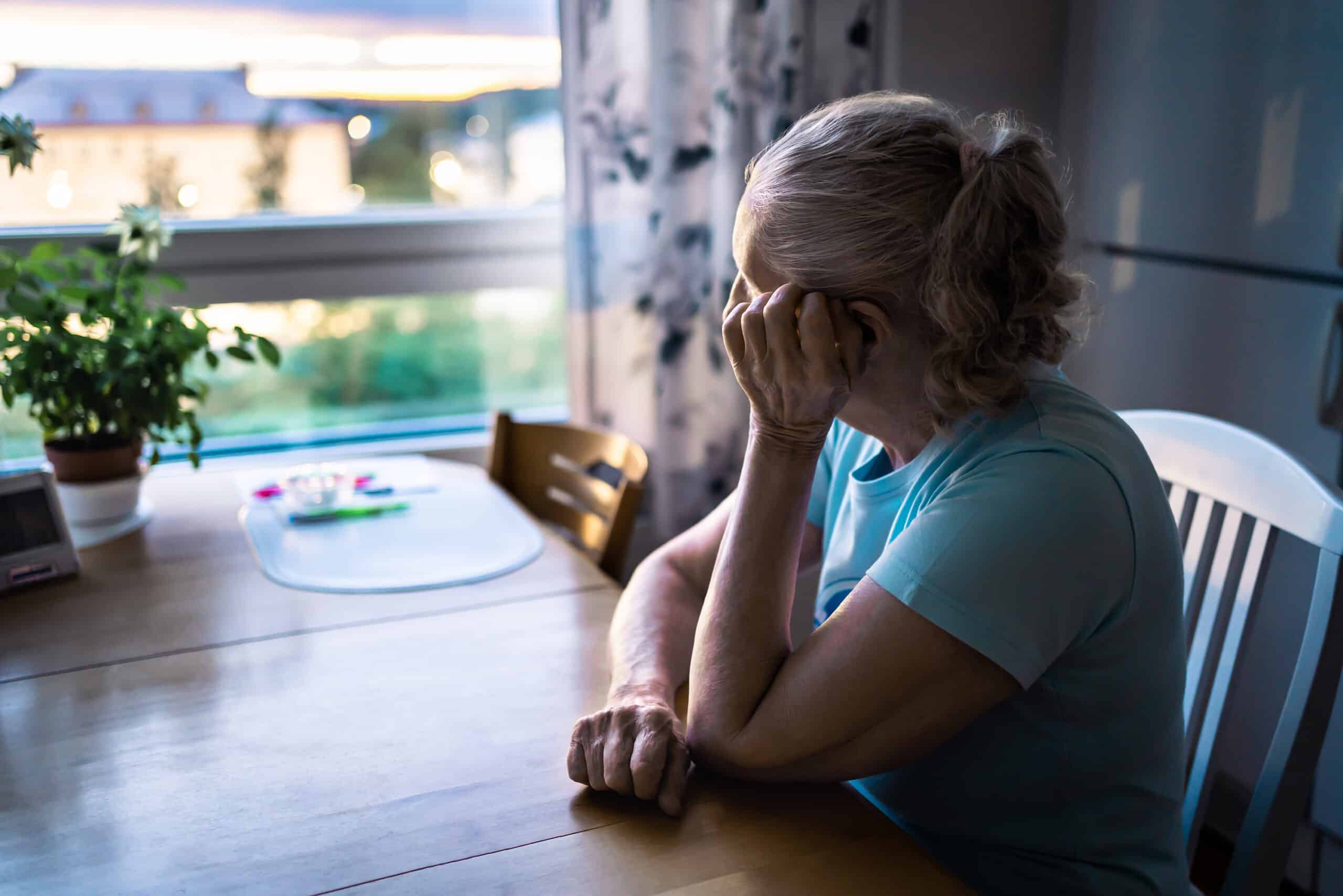 A lonely senior woman living on her own and looking out the window longingly.