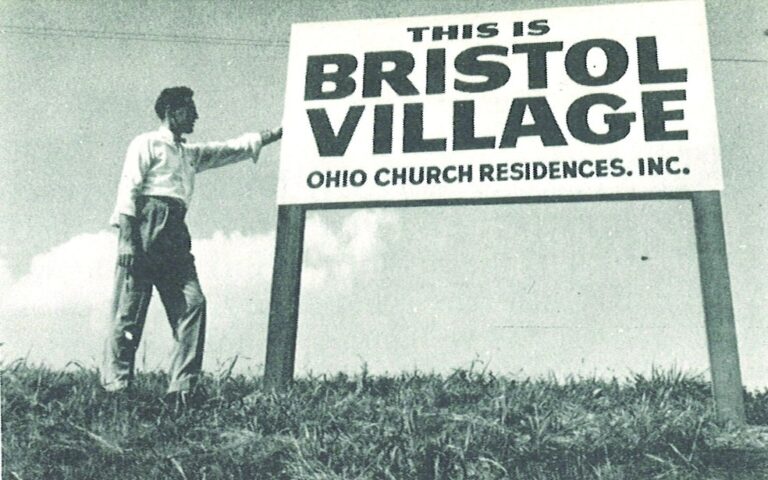 John Glen posing with original Bristol Village sign.