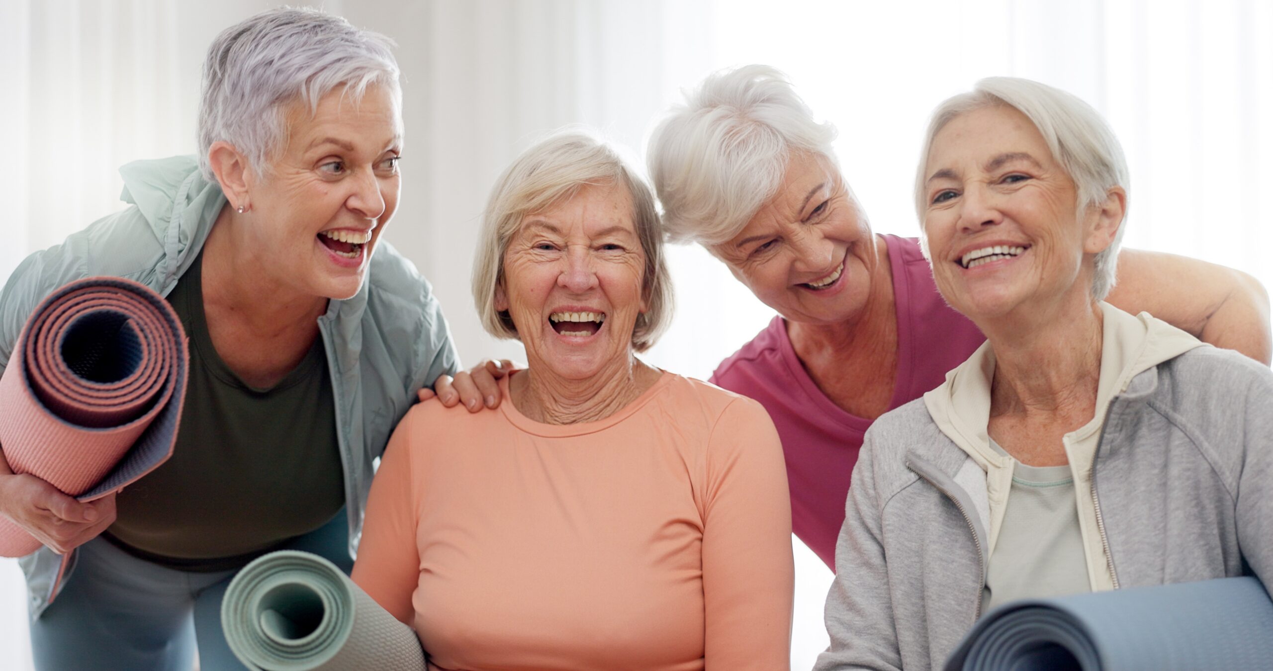 Four smiling senior women holding yoga mats after a class