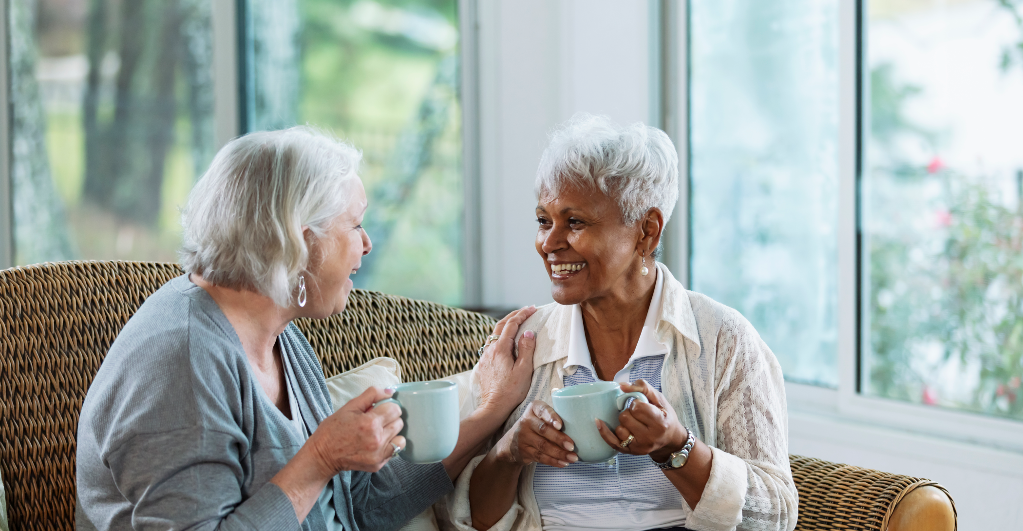 two senior females sitting on a couch drinking tea