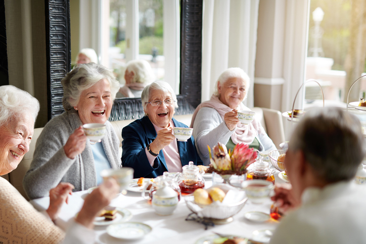 Group of senior women laughing and enjoying afternoon tea at a table