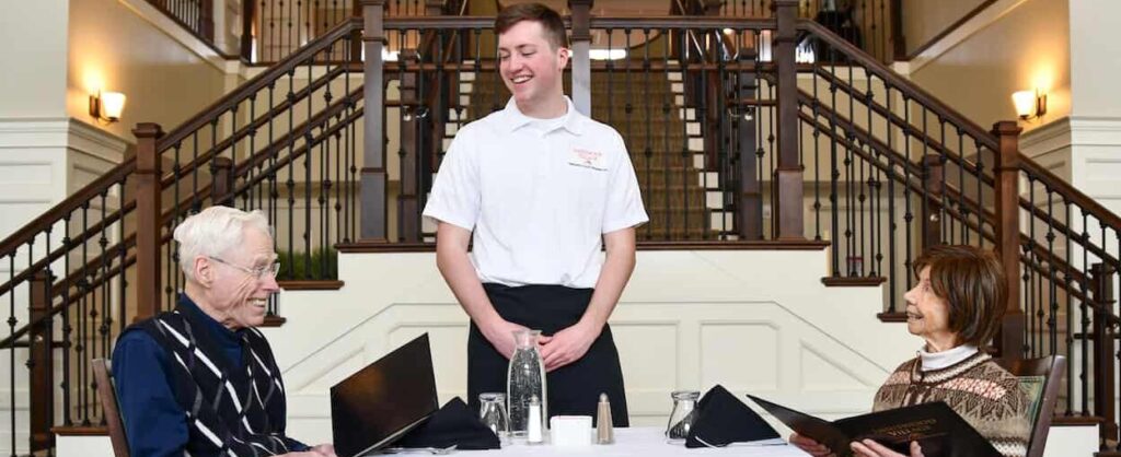 Server smiling at two seniors dining in a grand room