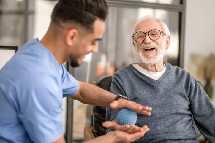 Caregiver helping a smiling senior man with a blue stress ball