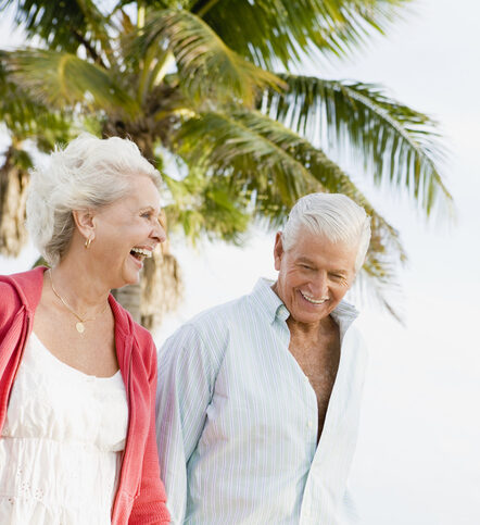 Happy senior couple walking outdoors by palm tree