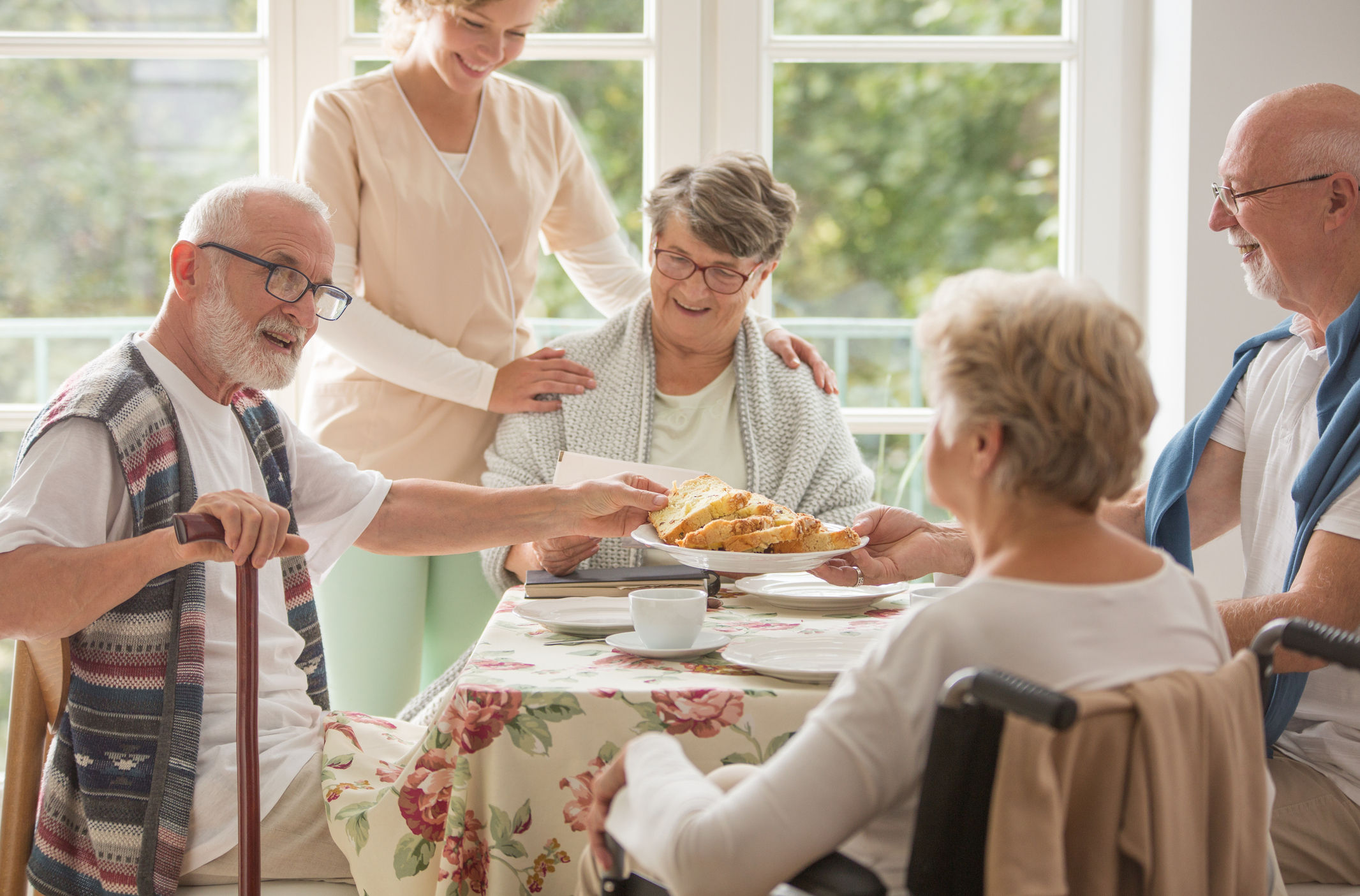 Caregiver serving food to a group of smiling seniors at a table