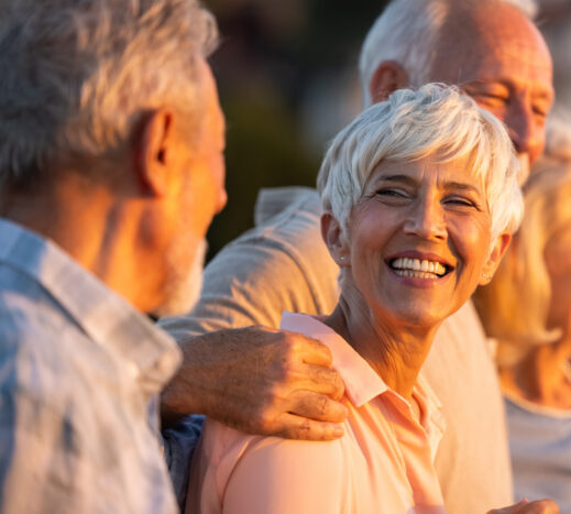 Happy senior woman smiling with friends at sunset