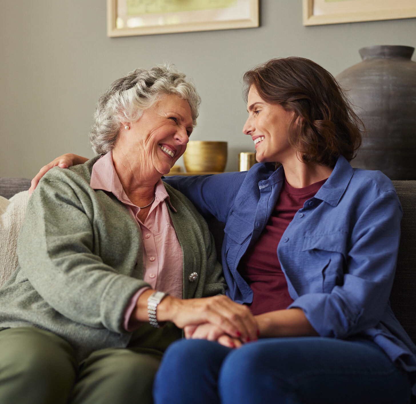 Senior woman and adult daughter smiling on a couch