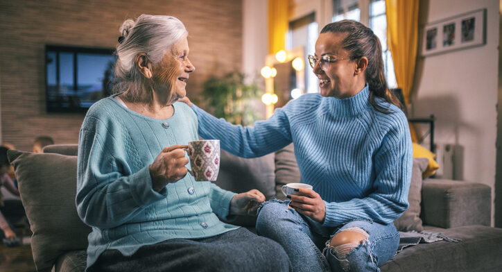 Caregiver and senior woman smiling while having tea on a couch