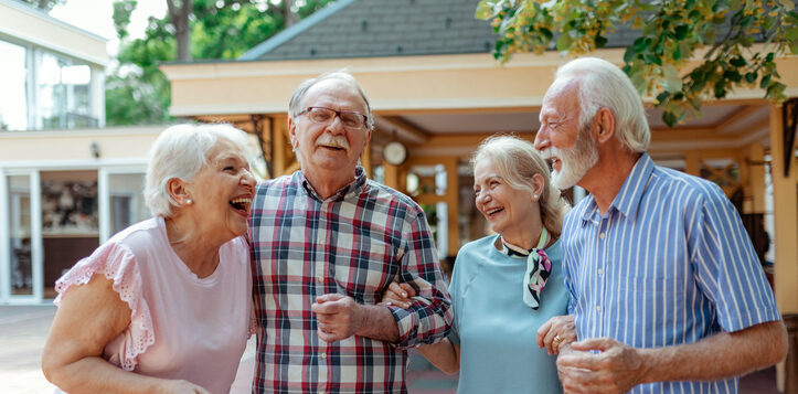 Four seniors laughing and walking arm-in-arm outdoors