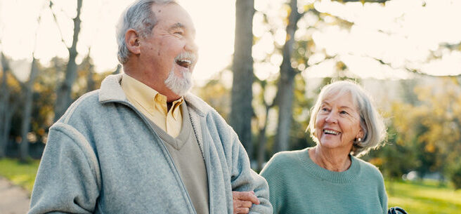 Happy senior couple walking arm-in-arm outdoors holding coffee cups