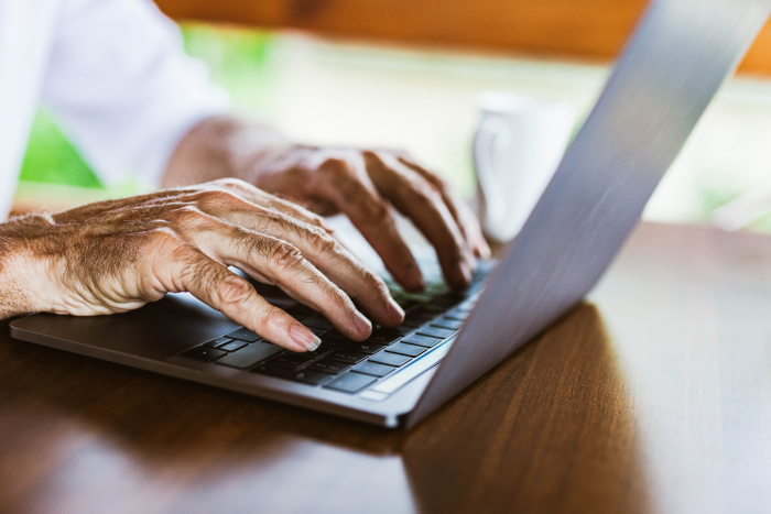senior hands typing on a laptop