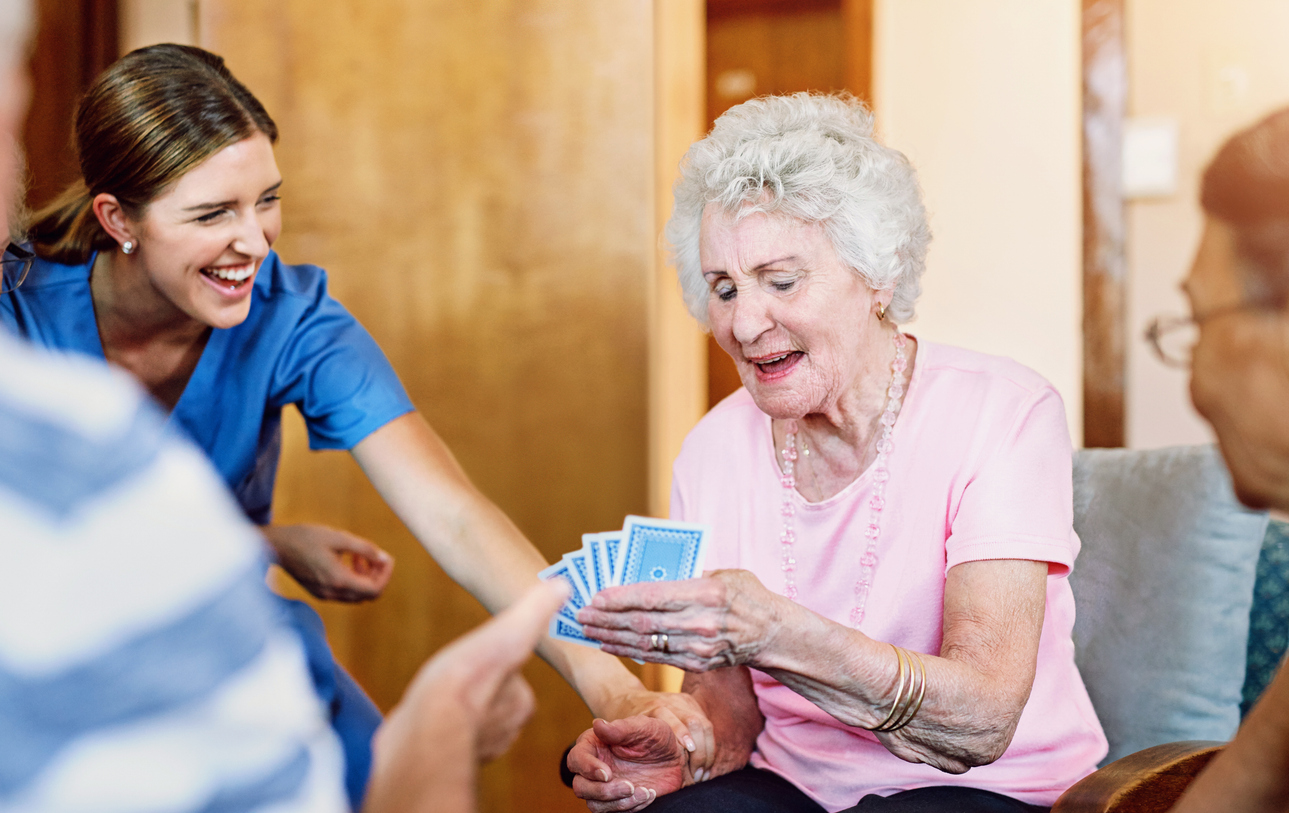 Caregiver and senior woman playing cards and laughing