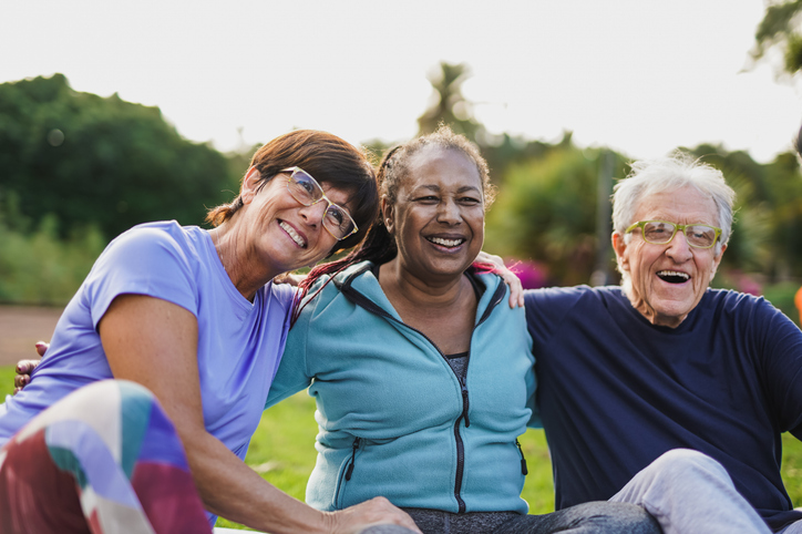 Three diverse seniors laughing and sitting together outdoors in a park