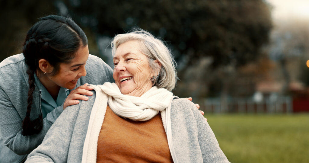 Young caregiver smiling with a happy senior woman outdoors
