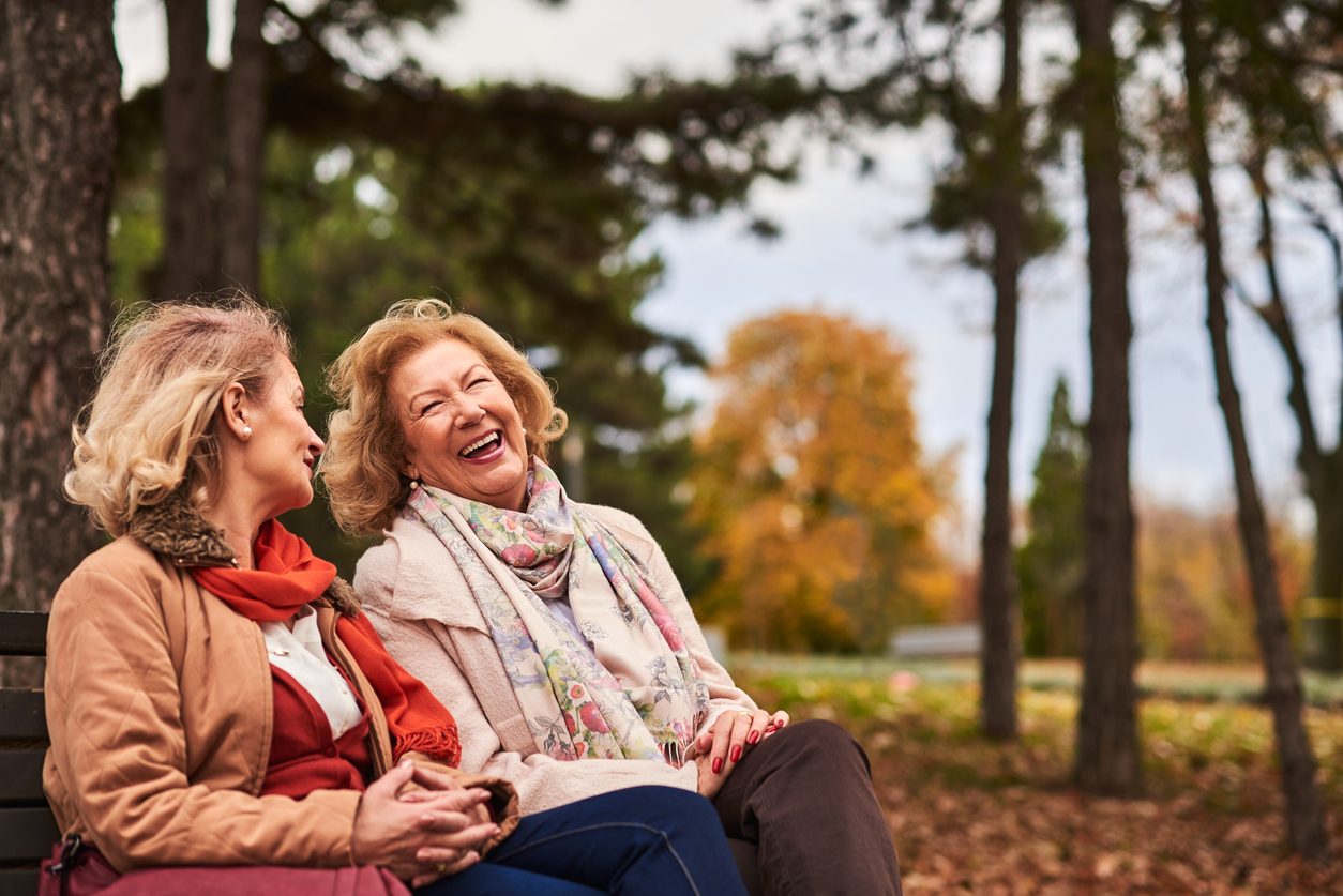 Two senior women laughing on a park bench