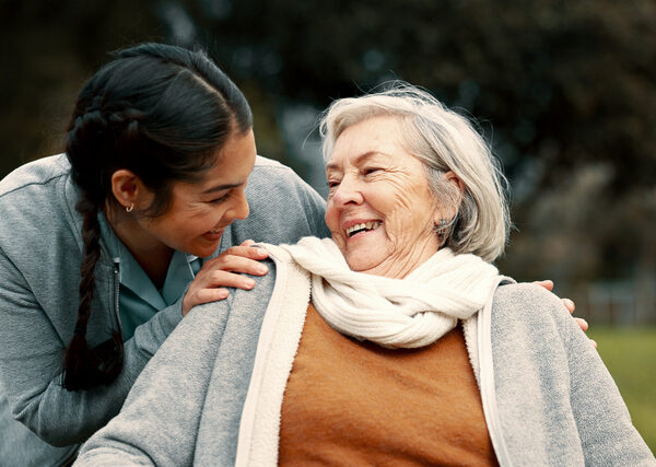 Caregiver helping woman with disability in park for support, trust and care in retirement. Nurse talking to happy senior patient in wheelchair for rehabilitation, therapy and conversation in garden