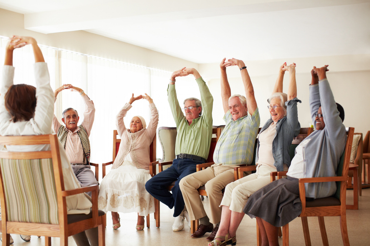 Group of seniors participating in chair exercise class with arms raised