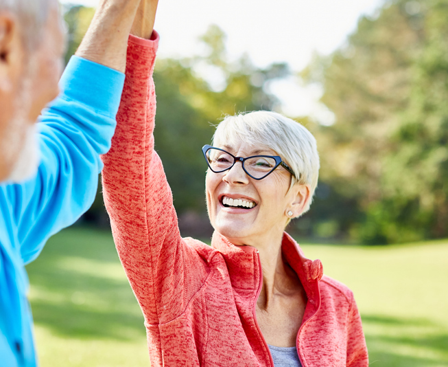Smiling active senior couple jogging exercising and having fun and giving high five together taking a break in the park