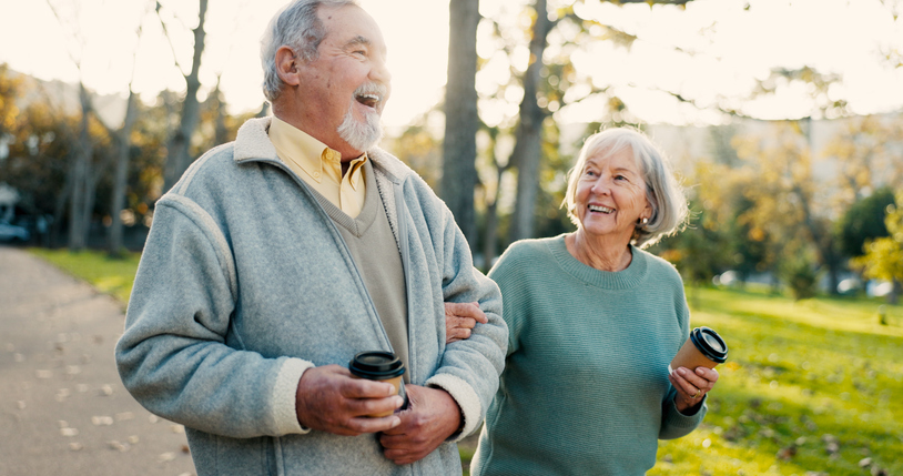 Happy senior couple walking arm-in-arm outdoors holding coffee cups