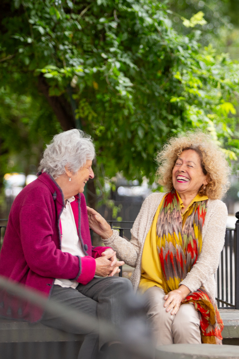 Two senior women laughing on a park bench