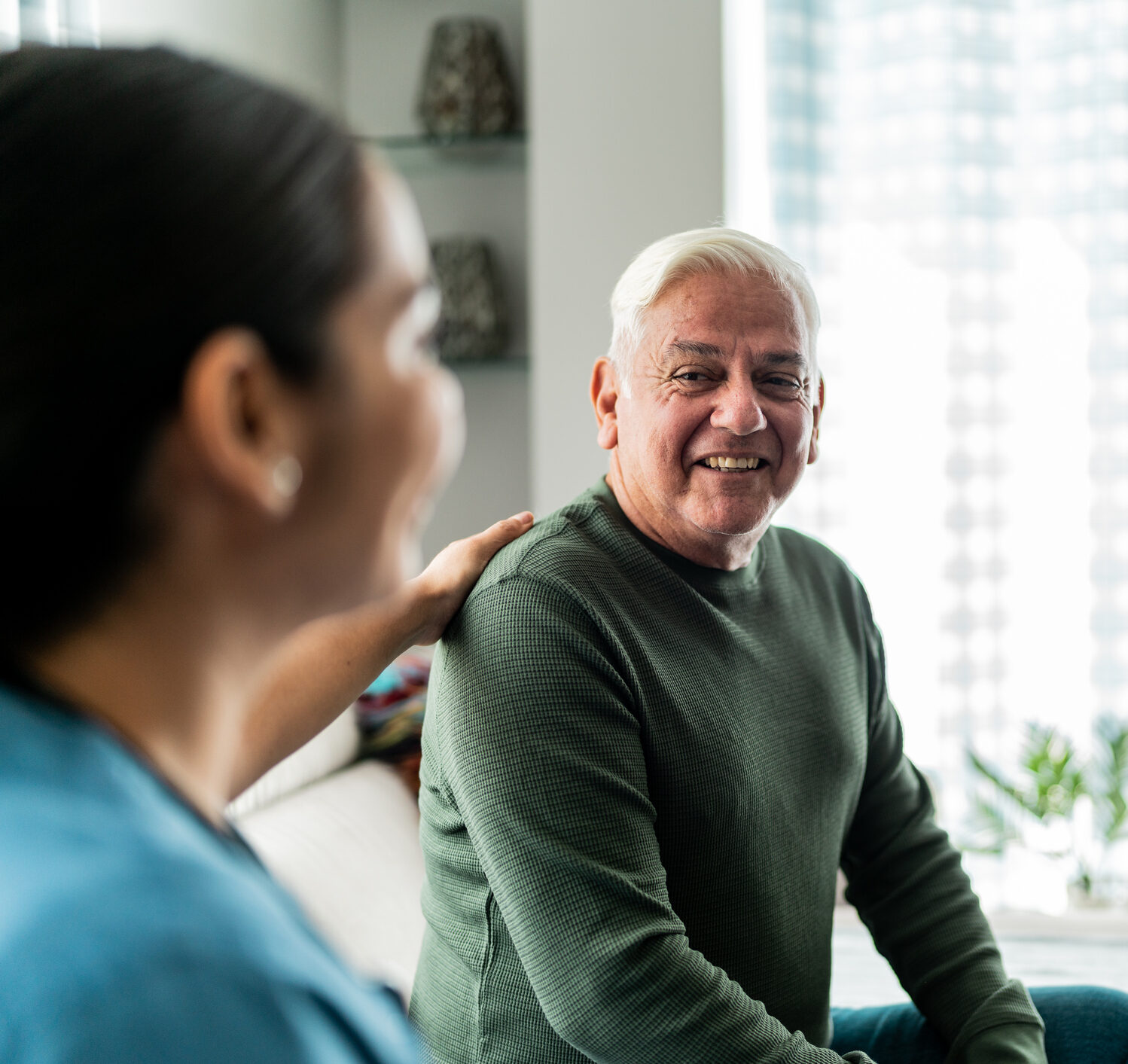 Senior man smiling at a caregiver with a hand on his shoulder