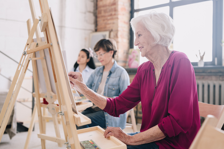 Senior woman painting on an easel in an art class with others