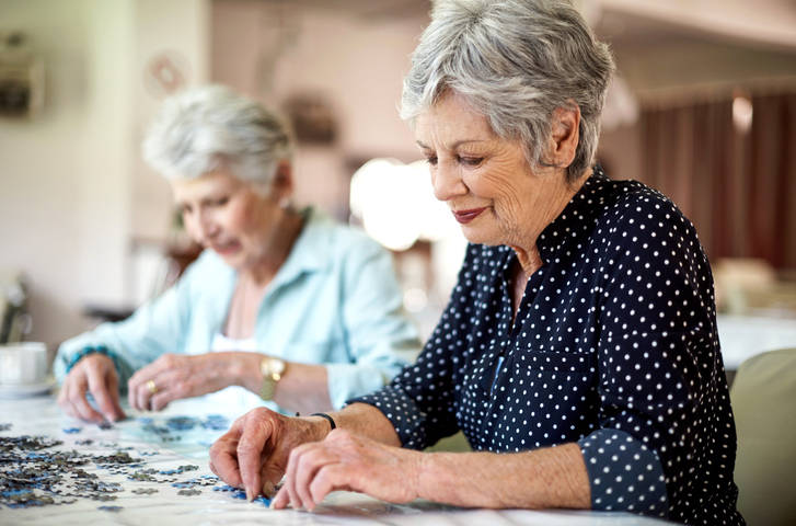 Two senior women concentrating on a jigsaw puzzle at a table