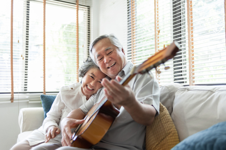 Senior Couple enjoying singing and playing acoustic guitar together on sofa at home.