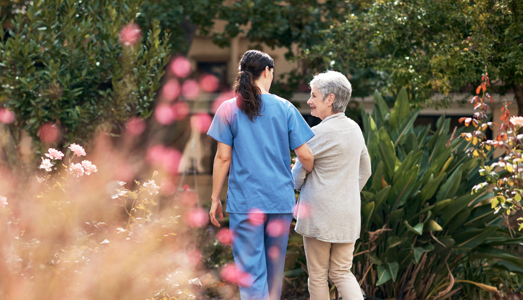 Caregiver and senior woman walking arm-in-arm in a garden