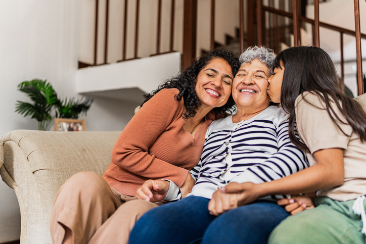 Senior woman receiving kisses from daughter and granddaughter at home