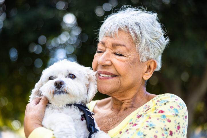 Senior woman holding a small white dog outdoors in a park