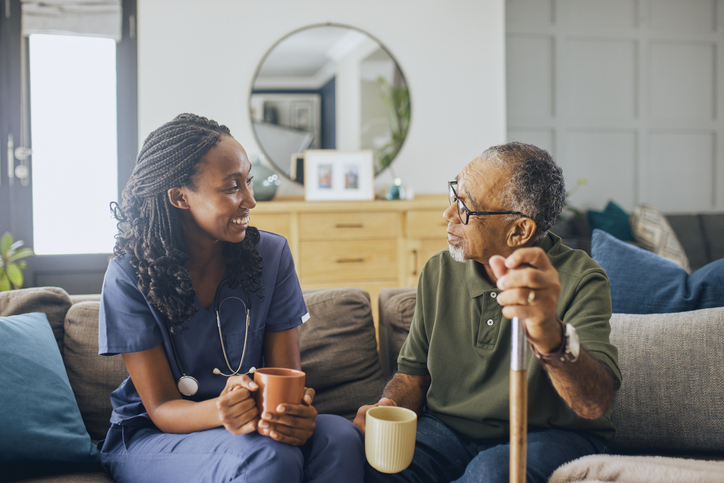 Caregiver and senior man with a cane talking on a couch