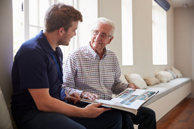Older man showing old photographs to a younger man, highlighting moments affected by memory loss