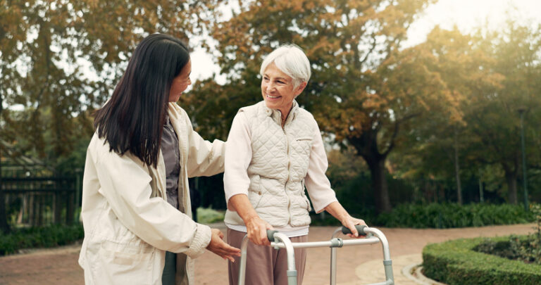 A caregiver and senior woman walk outside together, demonstrating the personal support you receive in assisted living vs. independent living