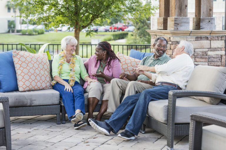 Group of senior friends talking together on an outdoor patio at a senior living community